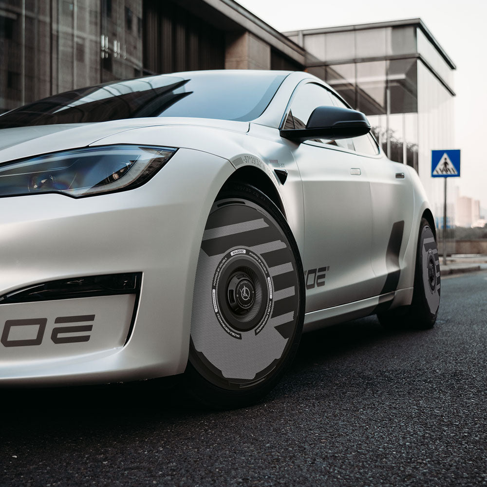 A white Tesla Model S with HALODISC 2 Wheel Covers by HALOBLK Store is parked near a modern glass building and a pedestrian crossing sign.