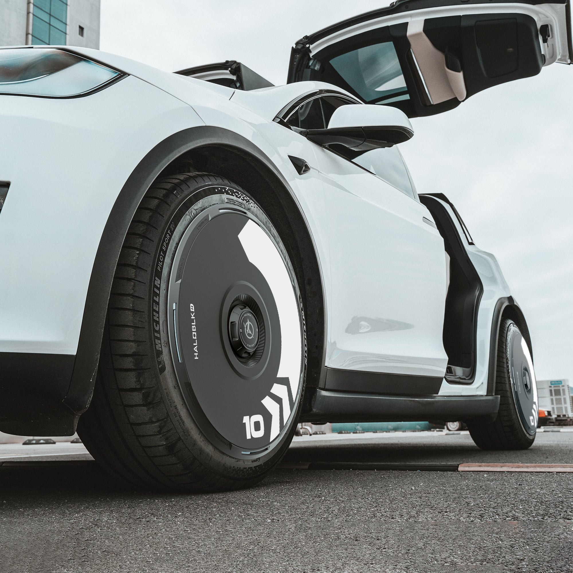 Close-up, low-angle view of a Tesla Model X (2021-2025) with open scissor doors, featuring HALODISC 2 Wheel Covers (20" Perihelix Wheels丨Arrow) from HALOBLK Store, in black and white on an urban street.