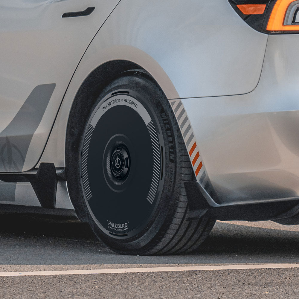 Close-up of a Tesla Model 3 Highland with HALODISC 2 Wheel Covers (Silver Track) from HALOBLK Store, showcasing a sleek black aerodynamic design with subtle text and patterns on the 19" Nova Wheels, parked on a paved surface.