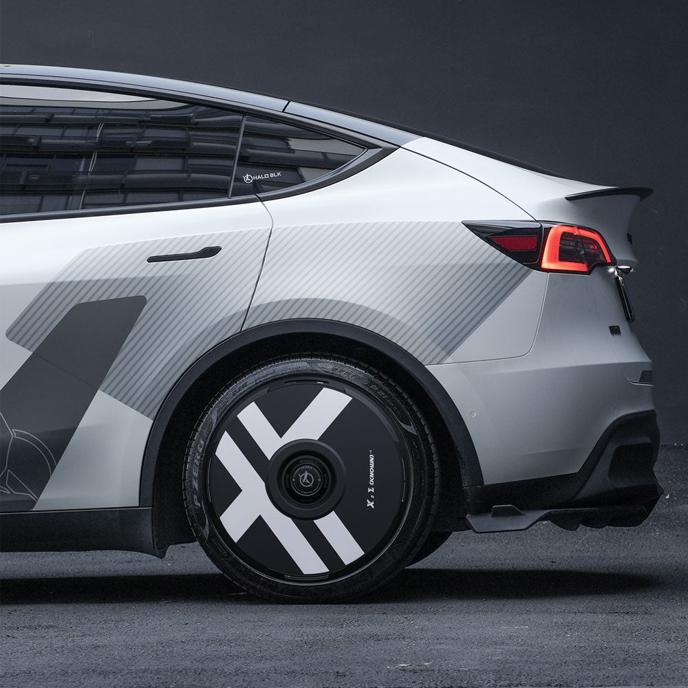 A close-up side view of a Tesla Model Y with HALODISC 2 Wheel Covers for 21" Überturbine Wheels by HALOBLK Store, featuring bold white “X” designs on custom black covers, parked against a dark background.