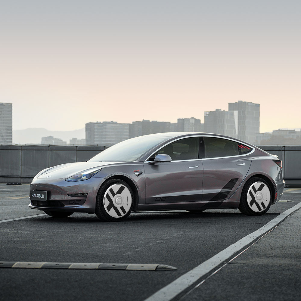 A Tesla Model 3 (2018-2023) with HALODISC 2 Wheel Covers by HALOBLK Store is parked on a rooftop against a city skyline, its unique X-Factor stiletto wheels standing out under a pale sky.