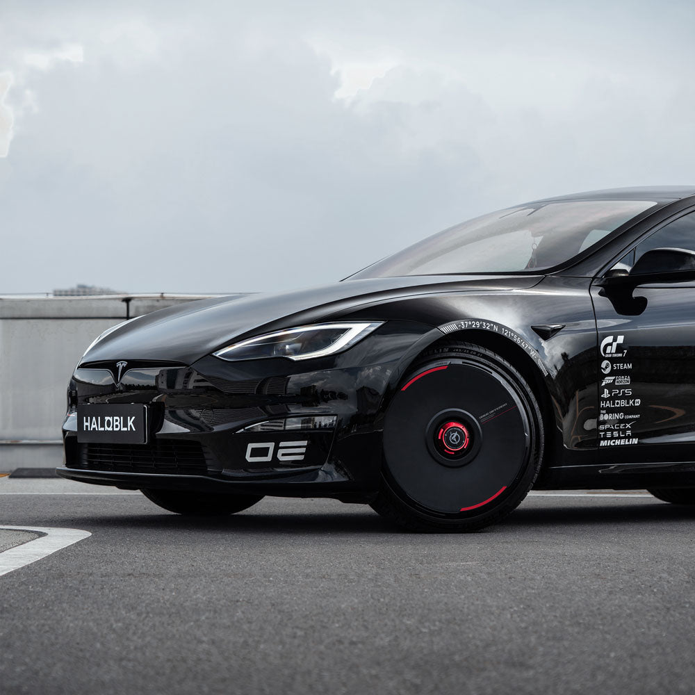 A stylish black Tesla Model S, featuring HALODISC 2 Wheel Covers for Tesla in Custom Numbers - Black from HALOBLK Store, is parked on a rooftop under a cloudy sky. The license plate reads HALO BLK.