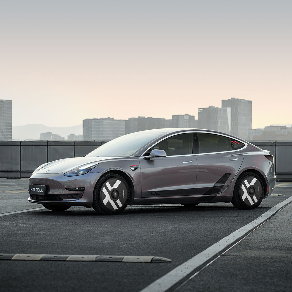 A gray Tesla Model 3 with HALODISC 2 Wheel Covers for 2018-2023 19" Stiletto Wheels by HALOBLK Store is parked on a rooftop, with a city skyline and mountains in the background.