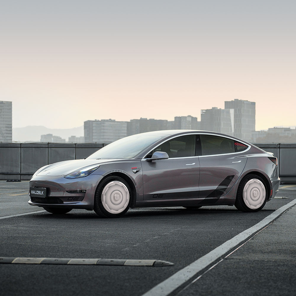 A silver sedan with HALODISC 2 Wheel Covers for Tesla Model 3 (2017-2018) 19" Performance Wheels by HALOBLK Store is parked on a rooftop with city buildings in the background under a clear sky.