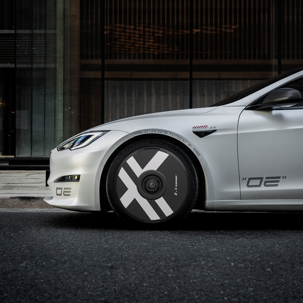 A Tesla Model S with HALODISC 2 Wheel Covers by HALOBLK Store, featuring black and gray geometric designs on the 21" Arachnid Wheels, is parked on a street in front of a modern glass building.