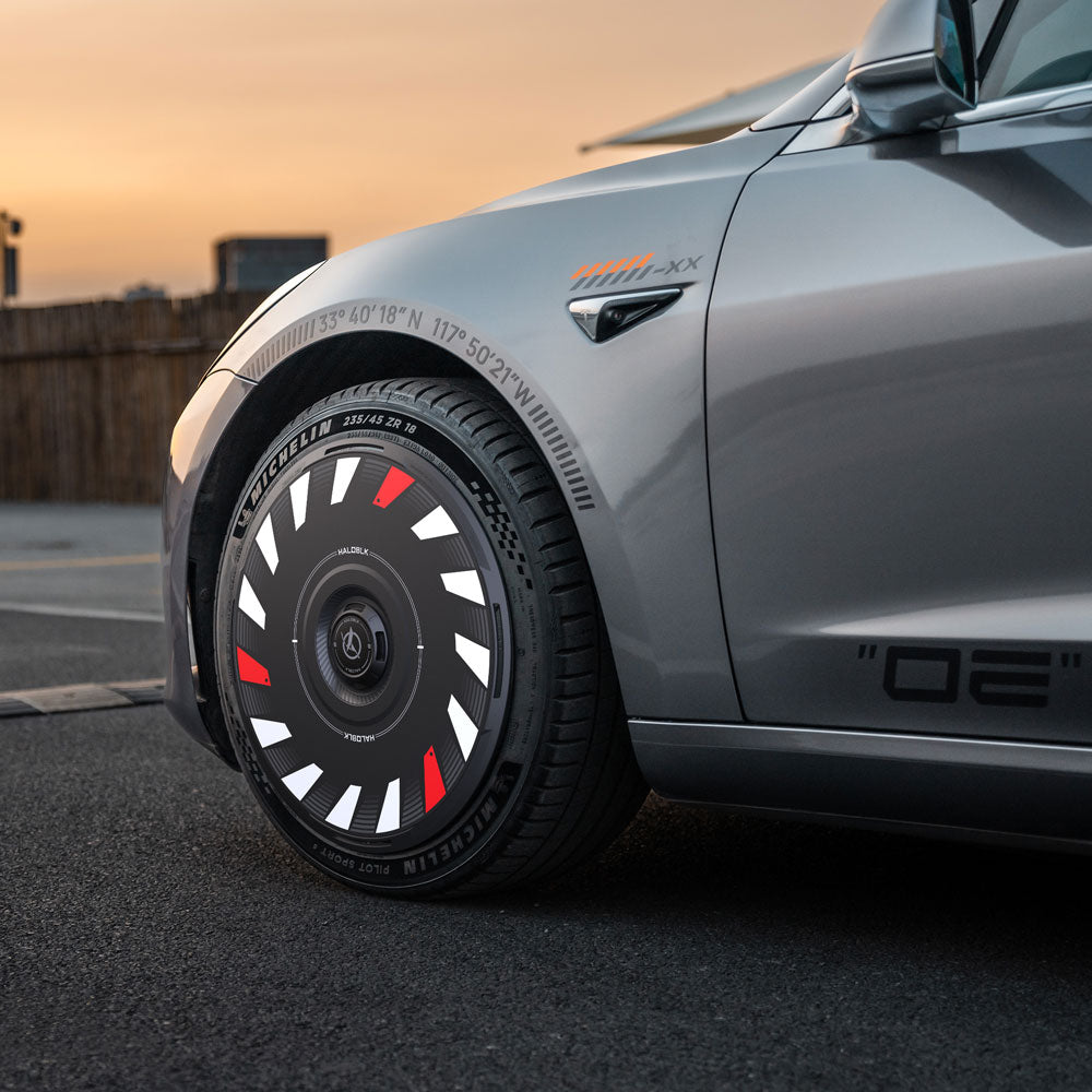 A close-up of HALODISC 2 Turbo Wheel Covers by HALOBLK Store, featuring illuminated red and white accents on a Tesla Model 3 2017–2023 with 18" Aero Wheels, attached to a silver car parked at sunset.