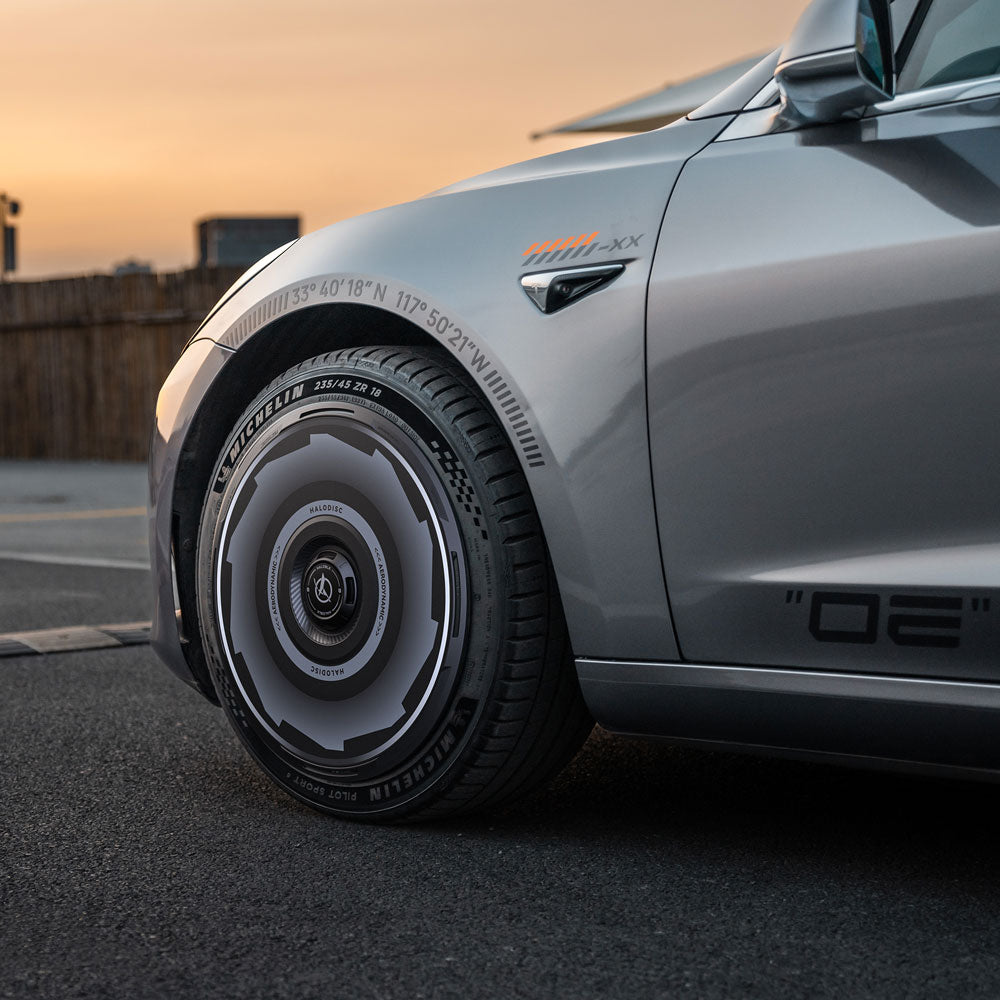 Close-up of a Tesla Model 3 (2019-2023) featuring HALOBLK Store's HALODISC 2 Wheel Covers for 19" Zero-G Wheels丨Vision-GT, with futuristic alloy design and Michelin tire, parked on a street at sunset. Partial car logo and stylish decals visible.