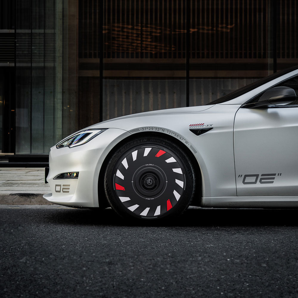 A silver Tesla Model S with HALODISC 2 Wheel Covers from HALOBLK Store on its 21" Turbine Wheels, sporting bold black covers with white and red accents. OE decals are on the bumper and door, set against a modern building facade.