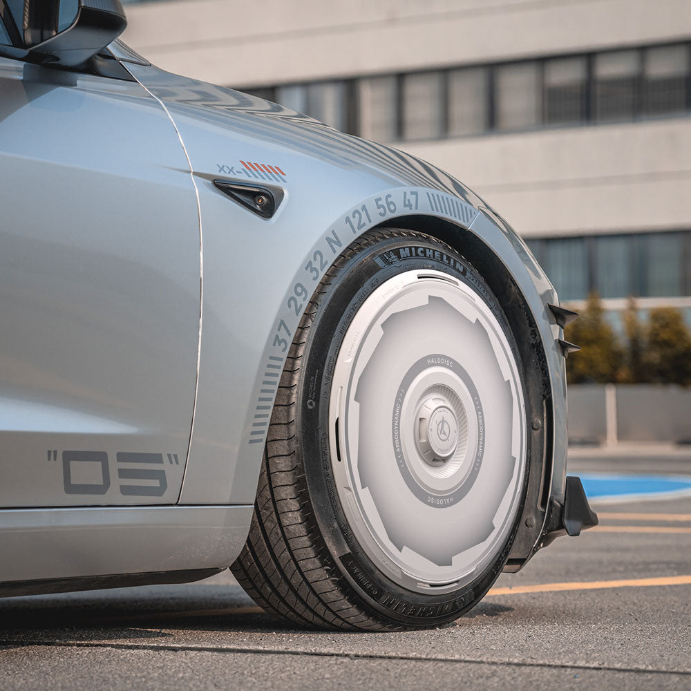 Close-up of a Tesla Model 3 Highland with HALODISC 2 Wheel Covers (Vision-GT, 19" Nova Wheels) from HALOBLK Store, showing futuristic smooth covers and detailed markings above the wheel in an urban setting with a modern building.