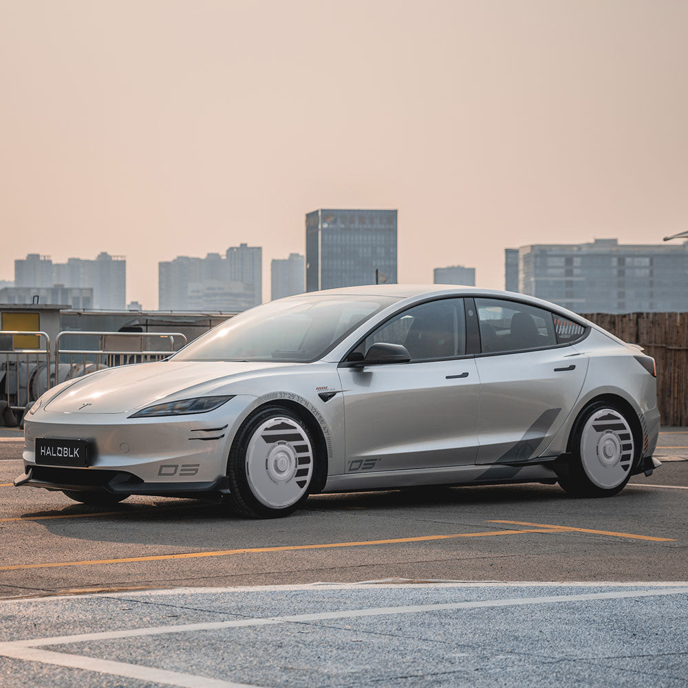 A sleek silver Tesla Model 3 Highland with HALODISC 2 Wheel Covers (19" Nova Wheels) from HALOBLK Store is parked on a rooftop, city buildings and a hazy sky in the background. The license plate reads “HALOBLK.”.