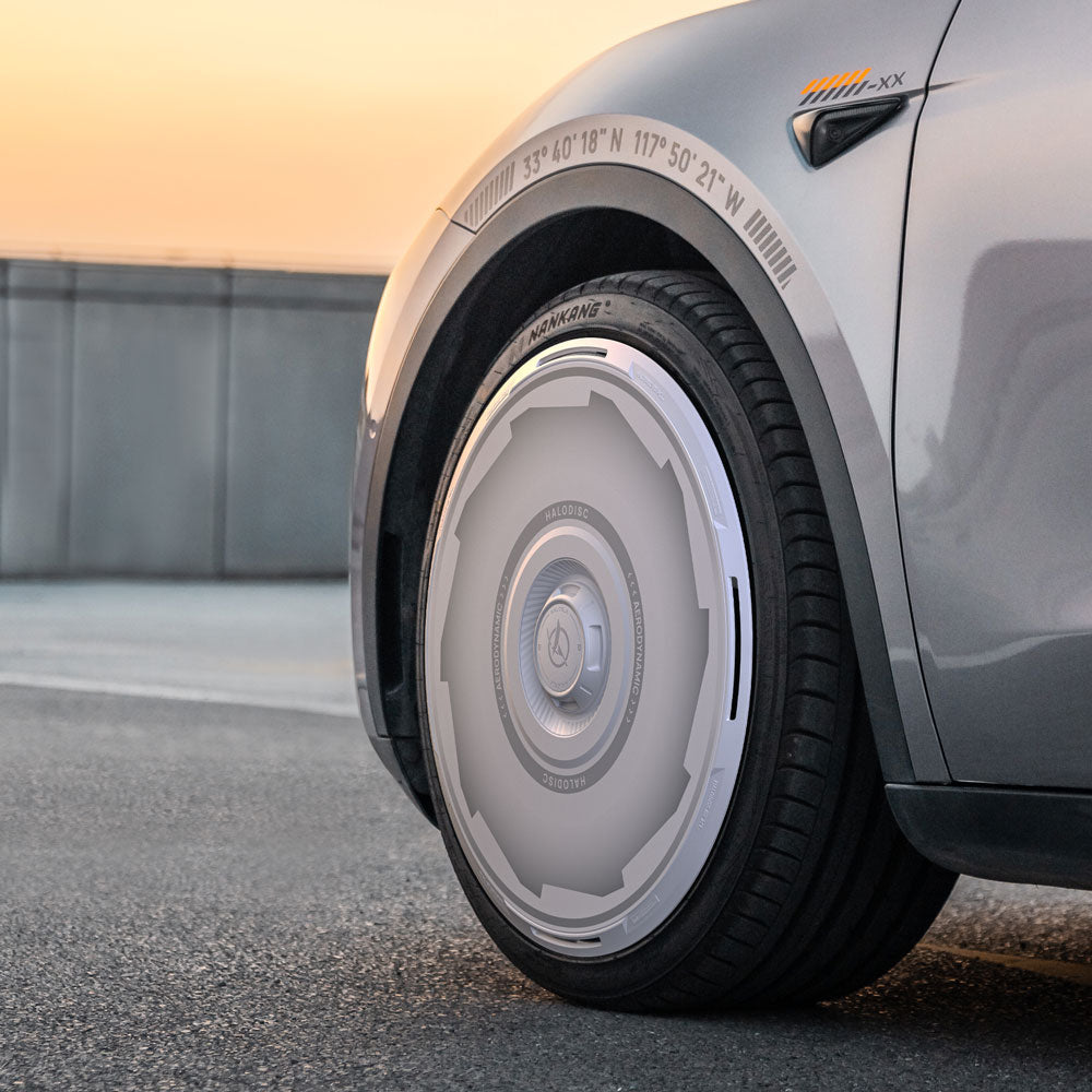 Close-up of HALODISC 2 Wheel Covers for Tesla Model Y 19" Gemini Wheels by HALOBLK Store, featuring a sleek, futuristic silver design with a smooth tire cover, showcased on a paved surface at sunset. Vision-GT edition.