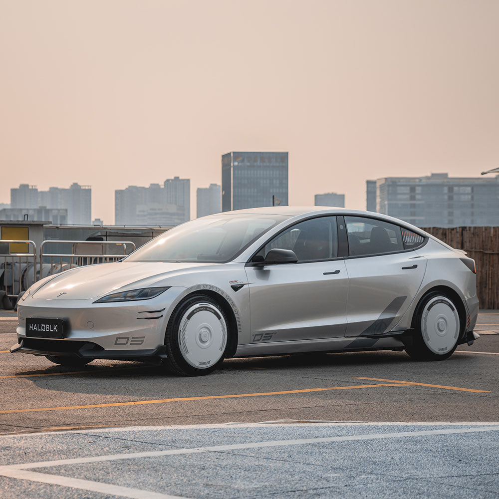 A Tesla Model 3 Highland with HALODISC 2 Silver Track 19" Nova Wheel Covers by HALOBLK Store is parked on a rooftop, city skyline and tall buildings visible in the hazy background.