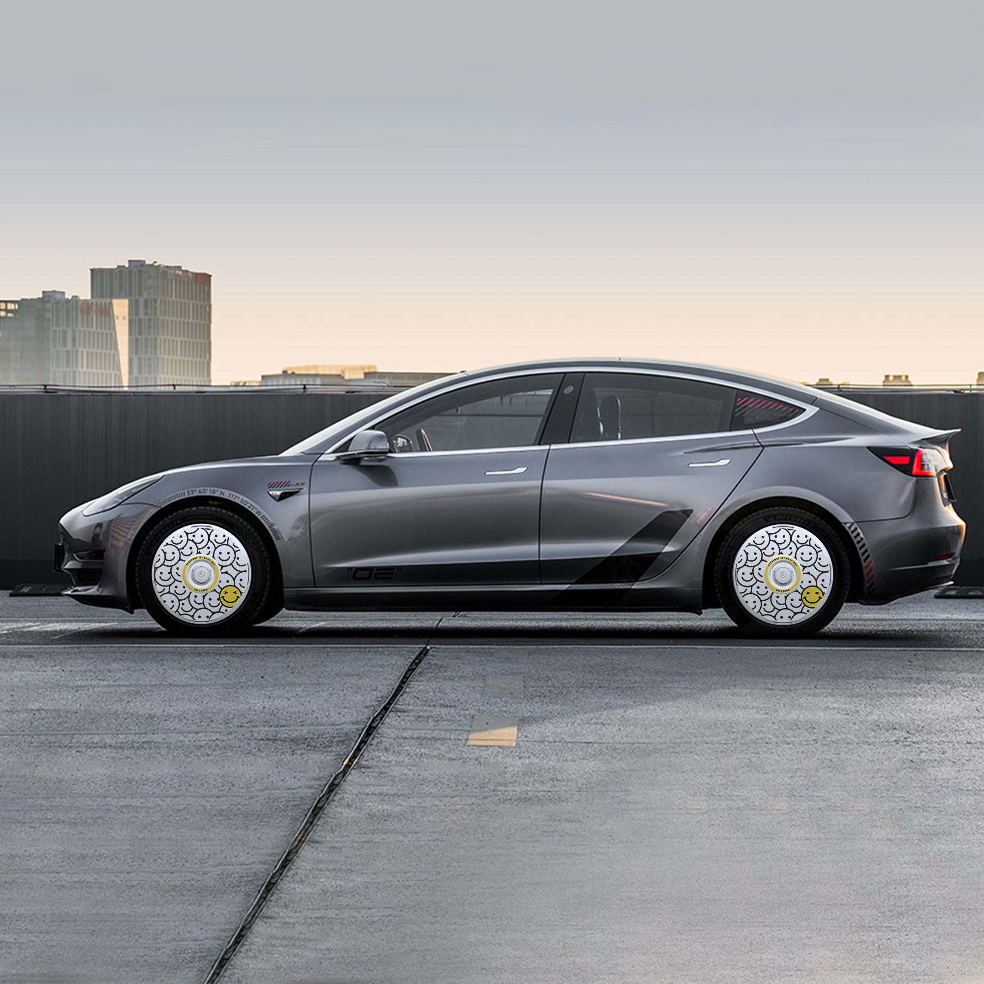 A silver sedan with HALODISC 2 Wheel Covers by HALOBLK Store for Tesla Model 3 (2017-2018) 19" Performance Wheels is parked on a rooftop, featuring white and yellow patterns, with tall buildings under a cloudy sky in the background.