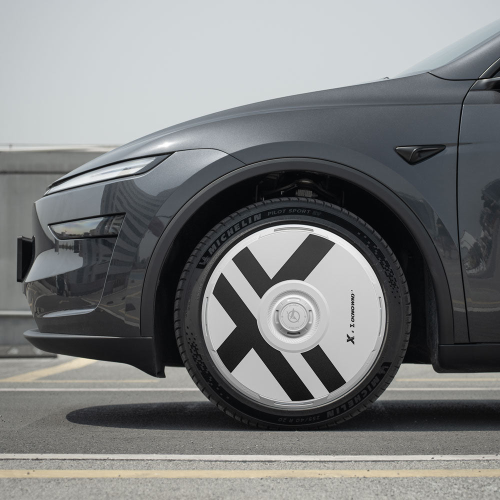Close-up of a Tesla Model Y's front left wheel fitted with HALODISC 2 X-Factor wheel covers from HALOBLK Store, designed for Juniper 20" Helix 2.0 wheels, showcasing bold black X-shaped graphics on a white cover.