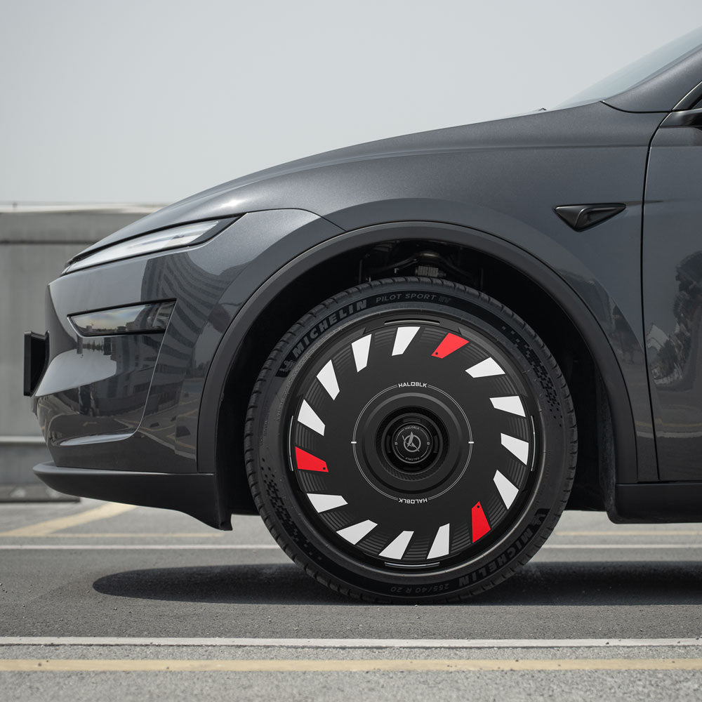 Close-up of a Tesla Model Y Juniper 20" Helix 2.0 wheel fitted with HALODISC 2 Wheel Covers by HALOBLK Store, showcasing bold black, white, and red geometric patterns, parked outdoors under clear skies.