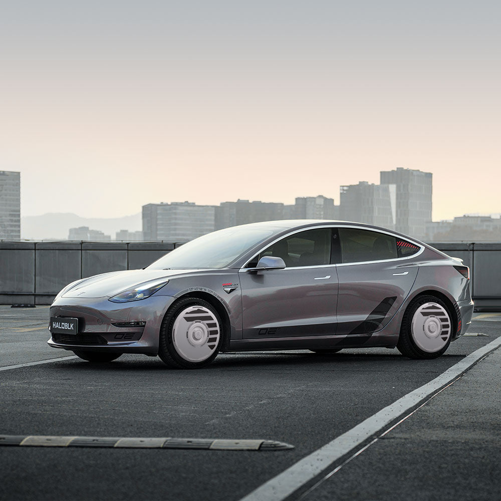 A Tesla Model 3 (2019-2023) with HALOBLK Store's HALODISC 2 Wheel Covers for 19" Sport Wheels is parked on a rooftop at dusk, city skyline and tall buildings in the background, showcasing the car’s futuristic look.