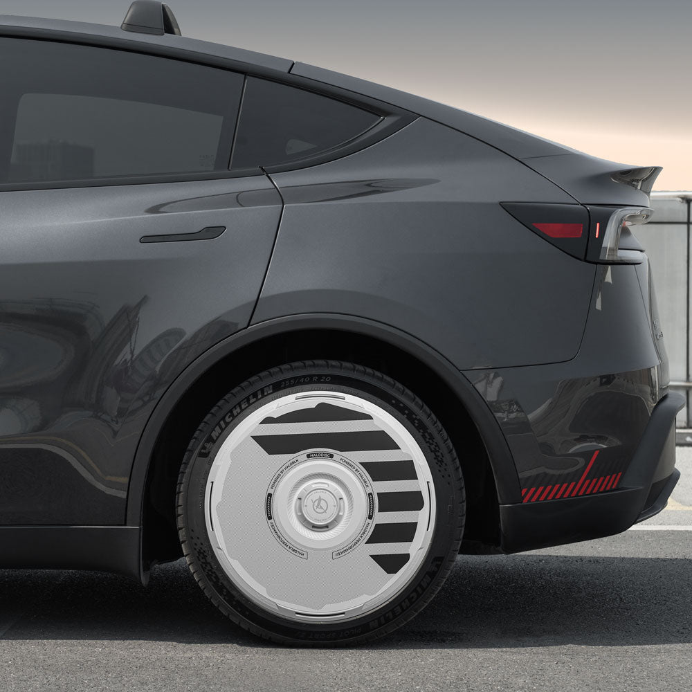 A close-up side view of a dark gray Tesla Model Y with HALODISC 2 Wheel Covers by HALOBLK Store, designed for the 19" Juniper Crossflow Wheels, showcasing their futuristic silver-and-black geometric pattern outdoors.