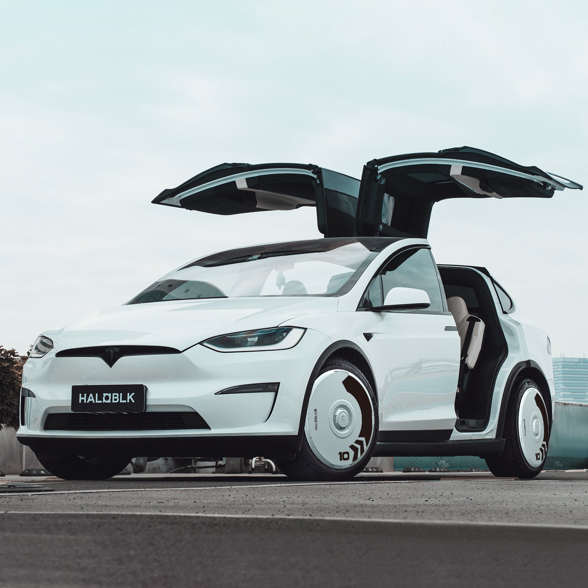 A white Tesla Model X (2016-2020) with HALODISC 2 Wheel Covers by HALOBLK Store on 20" Slipstream wheels sits outdoors with its falcon-wing doors open, custom rims visible, and a “HALOBLK” license plate.