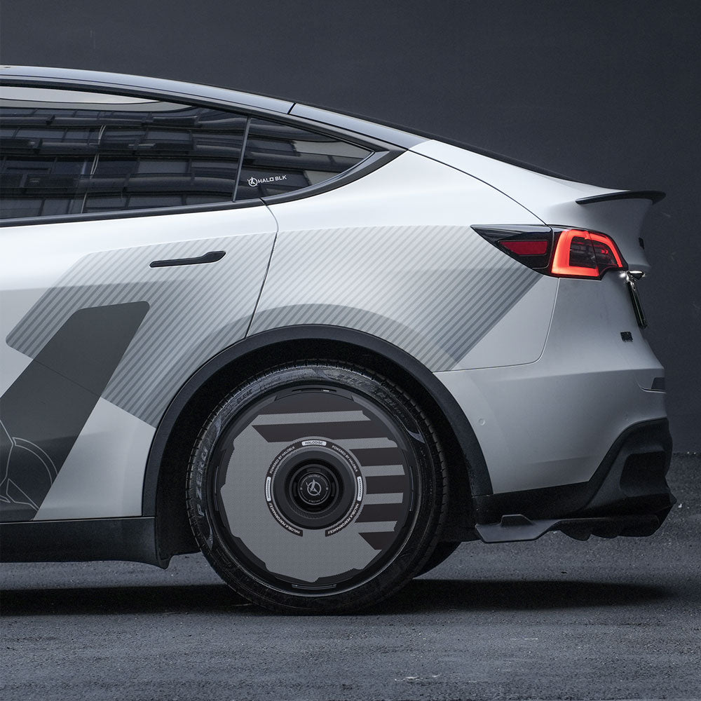 A close-up side view of a Tesla Model Y with HALODISC 2 Wheel Covers by HALOBLK Store on 19" Gemini wheels, highlighting the rear wheel and tail light, parked on a dark surface against a dark background.