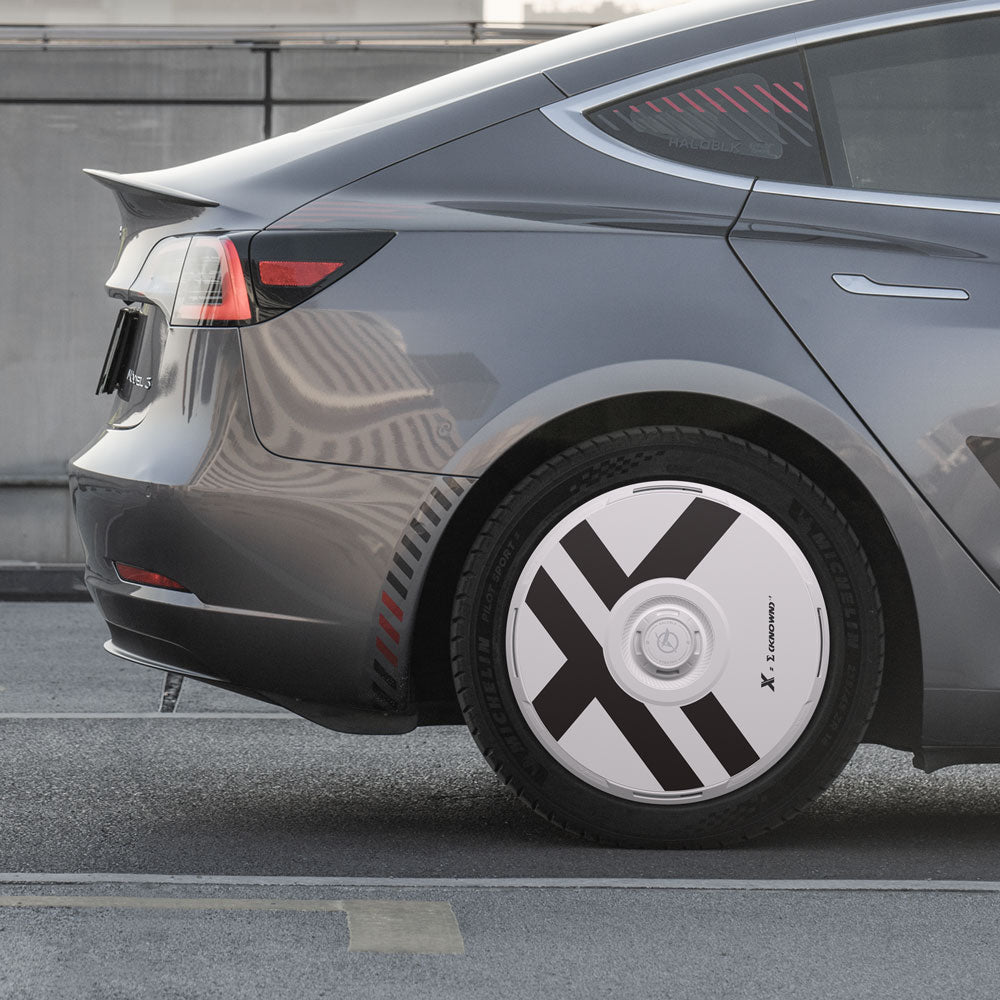A close-up of the rear of a gray Tesla Model 3 with HALODISC 2 Wheel Covers for 19" Stiletto Wheels by HALOBLK Store, featuring bold black X-shaped stripes and "X STROMER" text, parked on the street.