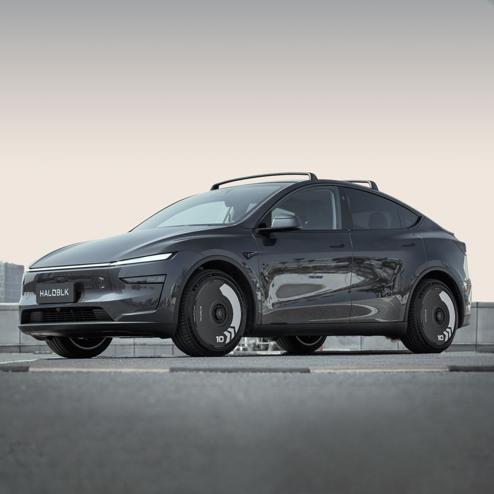 A black Tesla Model Y with HALODISC 2 Wheel Covers (Arrow, Helix 2.0, Juniper 20") from HALOBLK Store features sleek covered wheels and a modern aerodynamic design, parked outdoors on concrete with a light sky backdrop.