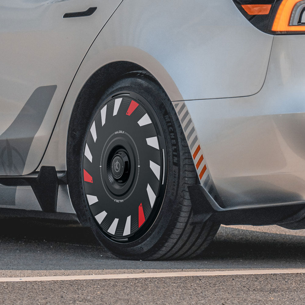 Close-up of a Tesla Model 3 Highland with HALODISC 2 Wheel Covers by HALOBLK Store on 18" Photon wheels, featuring black covers with white and red geometric accents. Silver-gray car, Michelin tire, taillight and fender visible.