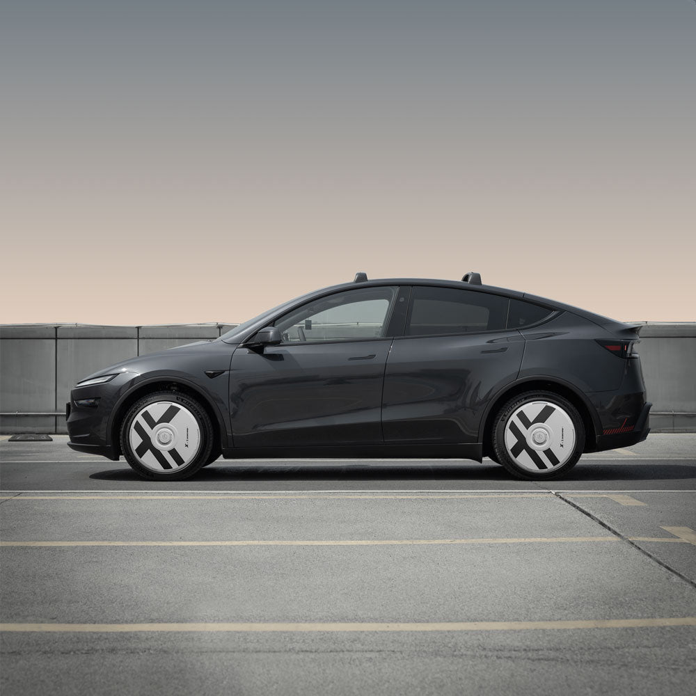 A Tesla Model Y with HALODISC 2 Wheel Covers by HALOBLK Store is parked in an empty outdoor lot, concrete barrier and gradient sky behind. The side view highlights the Juniper 20" Helix 2.0 Wheels’ X-Factor design.
