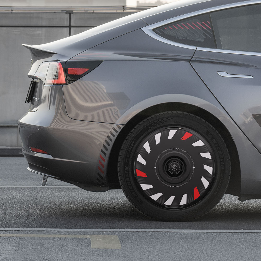 A close-up side view of a gray Tesla Model 3 (2017-2023) with HALODISC 2 Turbo 18" Aero Wheel Covers by HALOBLK Store, featuring unique black covers with red and white geometric accents.