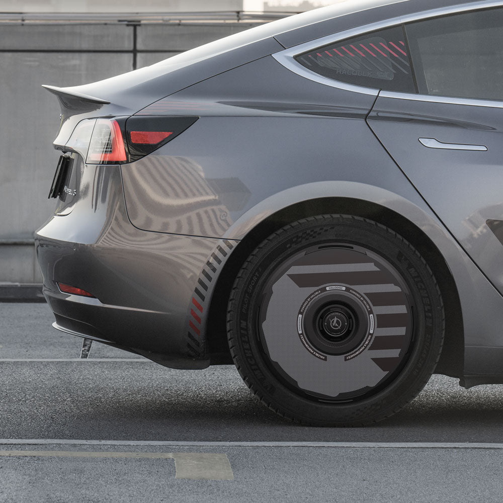 A close-up of the rear side of a gray Tesla Model 3 (2017-2023) with HALODISC 2 Wheel Covers by HALOBLK Store, showing the taillight, left rear wheel with sleek black H-Industry hubcaps, and part of the car’s smooth body.