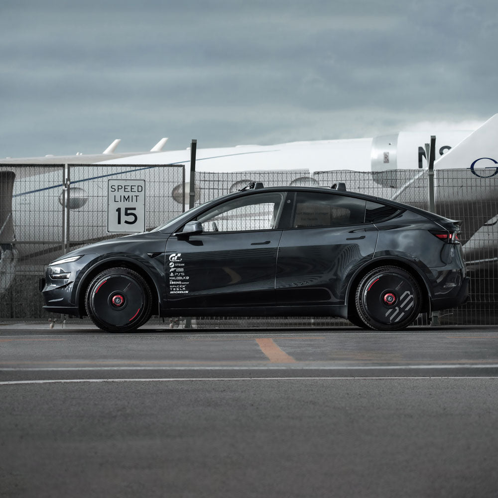 A Tesla Model Y featuring HALODISC 2 Wheel Covers for Tesla in black by HALOBLK Store, with custom numbers, is parked by a fence at an airport near an airplane and a Speed Limit 15 sign.
