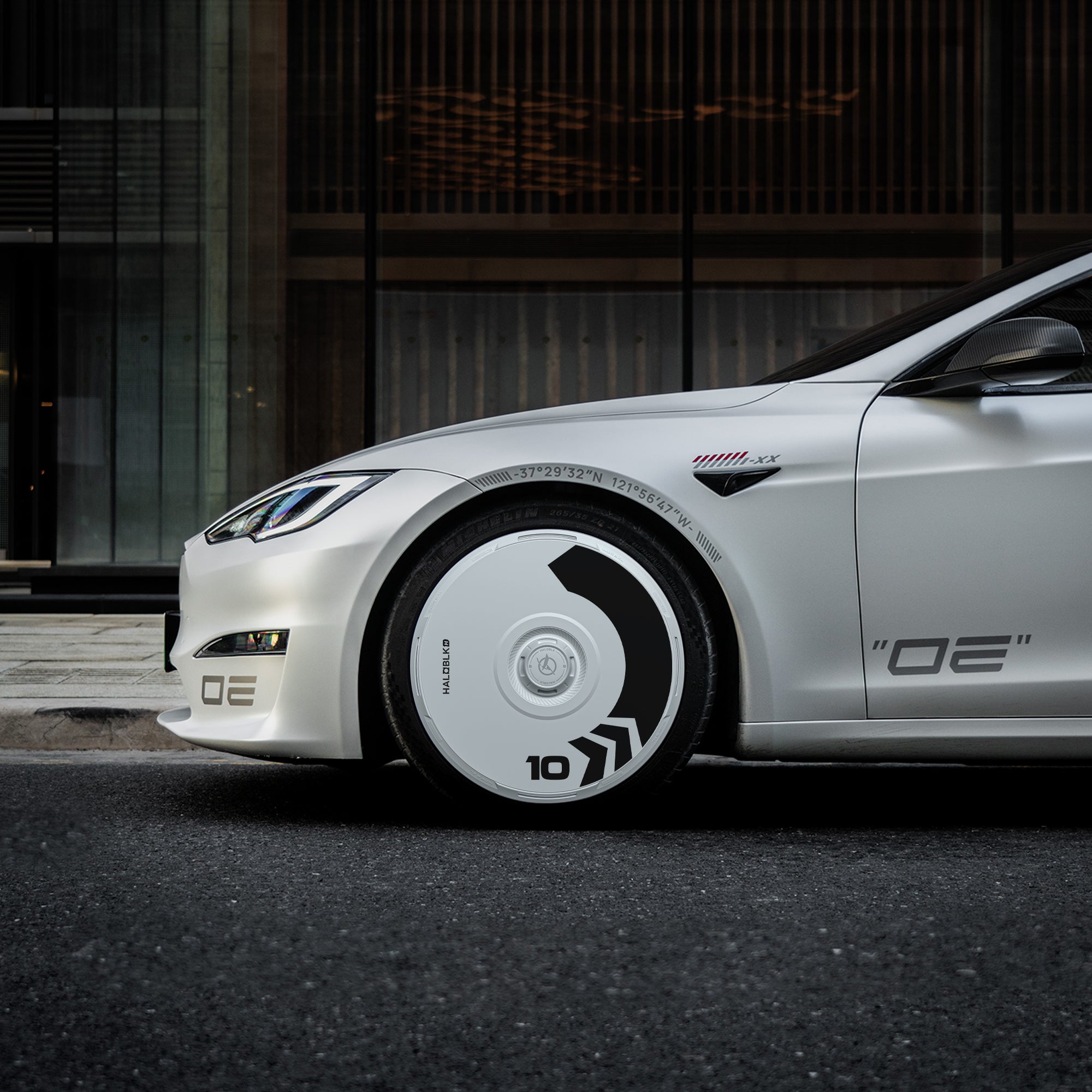 A white Tesla Model S with HALODISC 2 Wheel Covers (Arrow design) from HALOBLK Store, featuring bold black graphics and the number 10 on the front tire, OE decals, and a sleek, modern look parked on a city street.