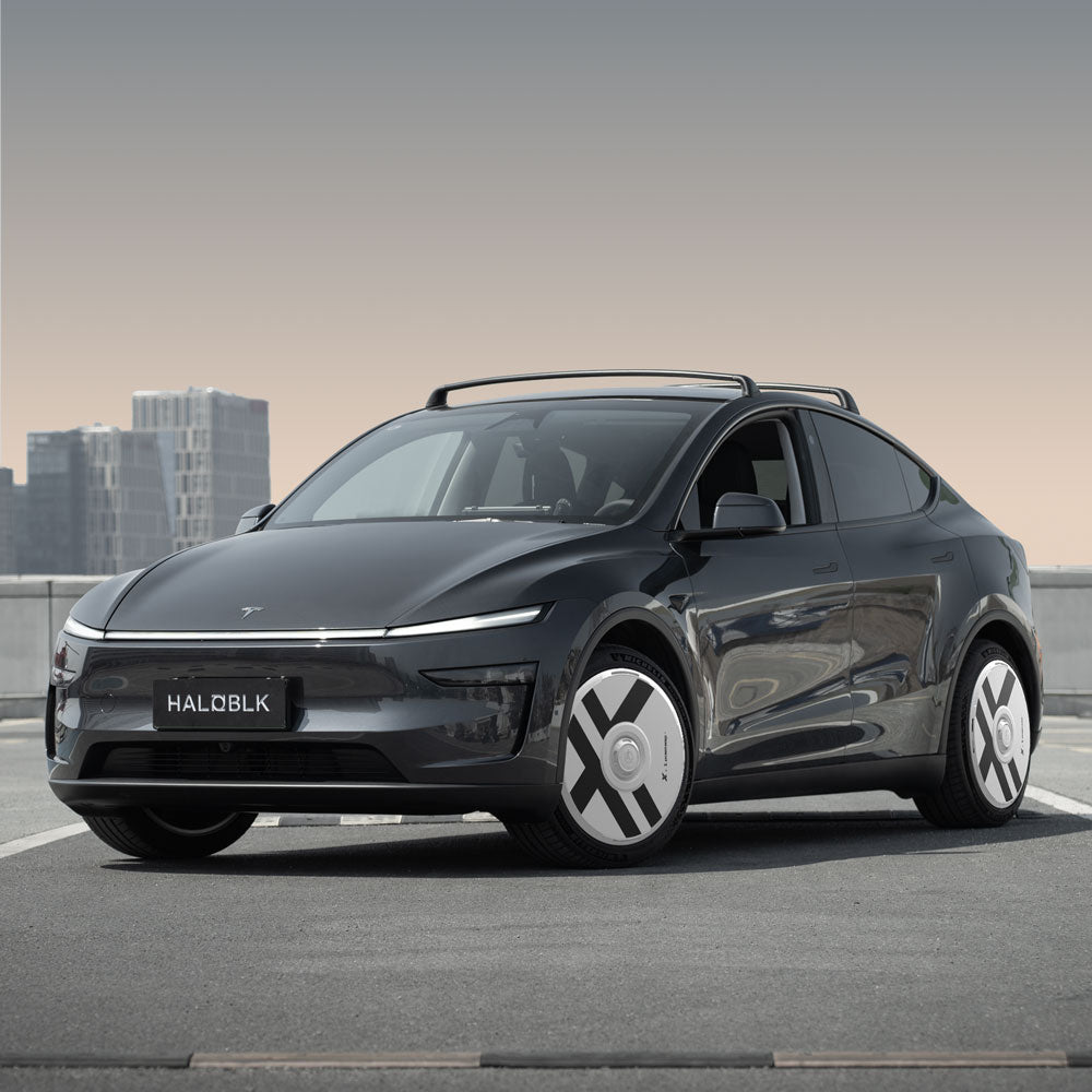 A Tesla Model Y with HALODISC 2 Wheel Covers by HALOBLK Store, designed for 20" Juniper Helix 2.0 wheels, is parked on a rooftop cityscape. The sleek black car features unique wheel covers and a HALOBLK license plate.