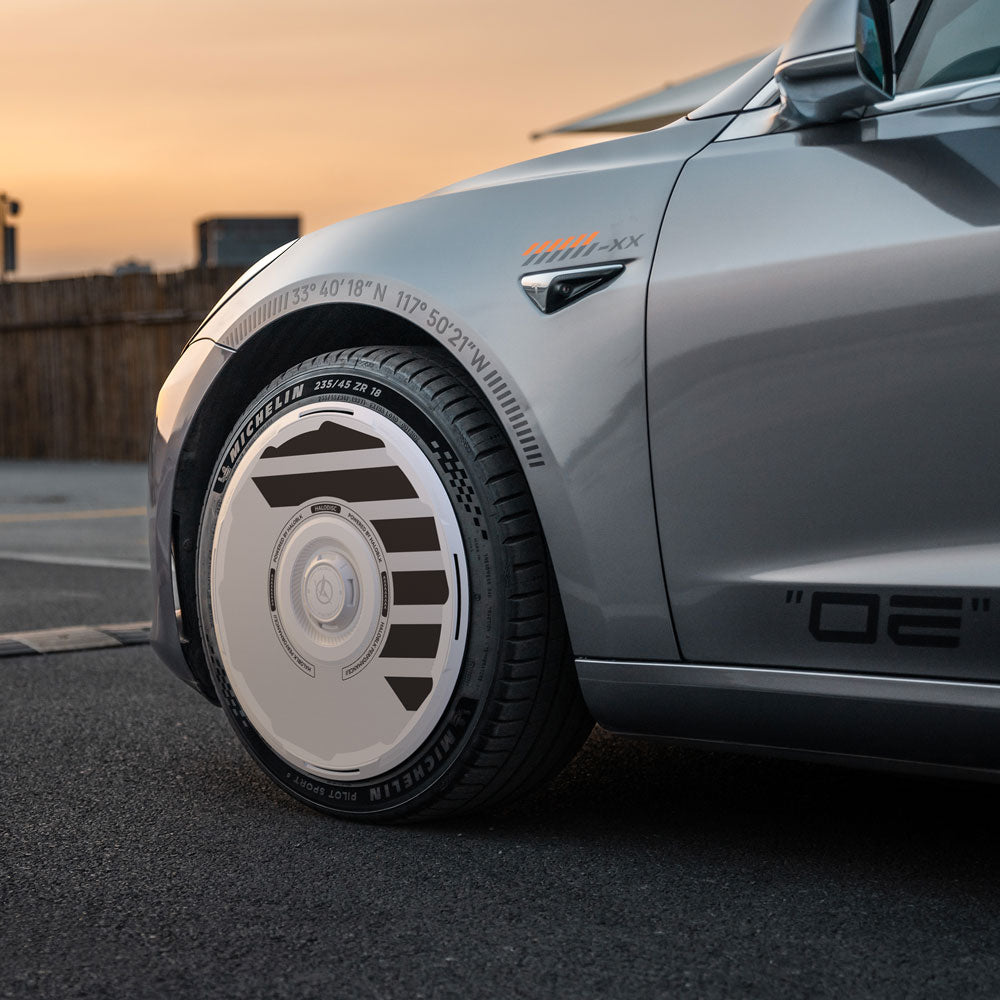 Close-up of a Tesla Model 3 (2018-2023) with HALODISC 2 Wheel Covers for 19" Stiletto Wheels by HALOBLK Store—sleek, aerodynamic white rim cover with dark geometric accents, parked at sunset.