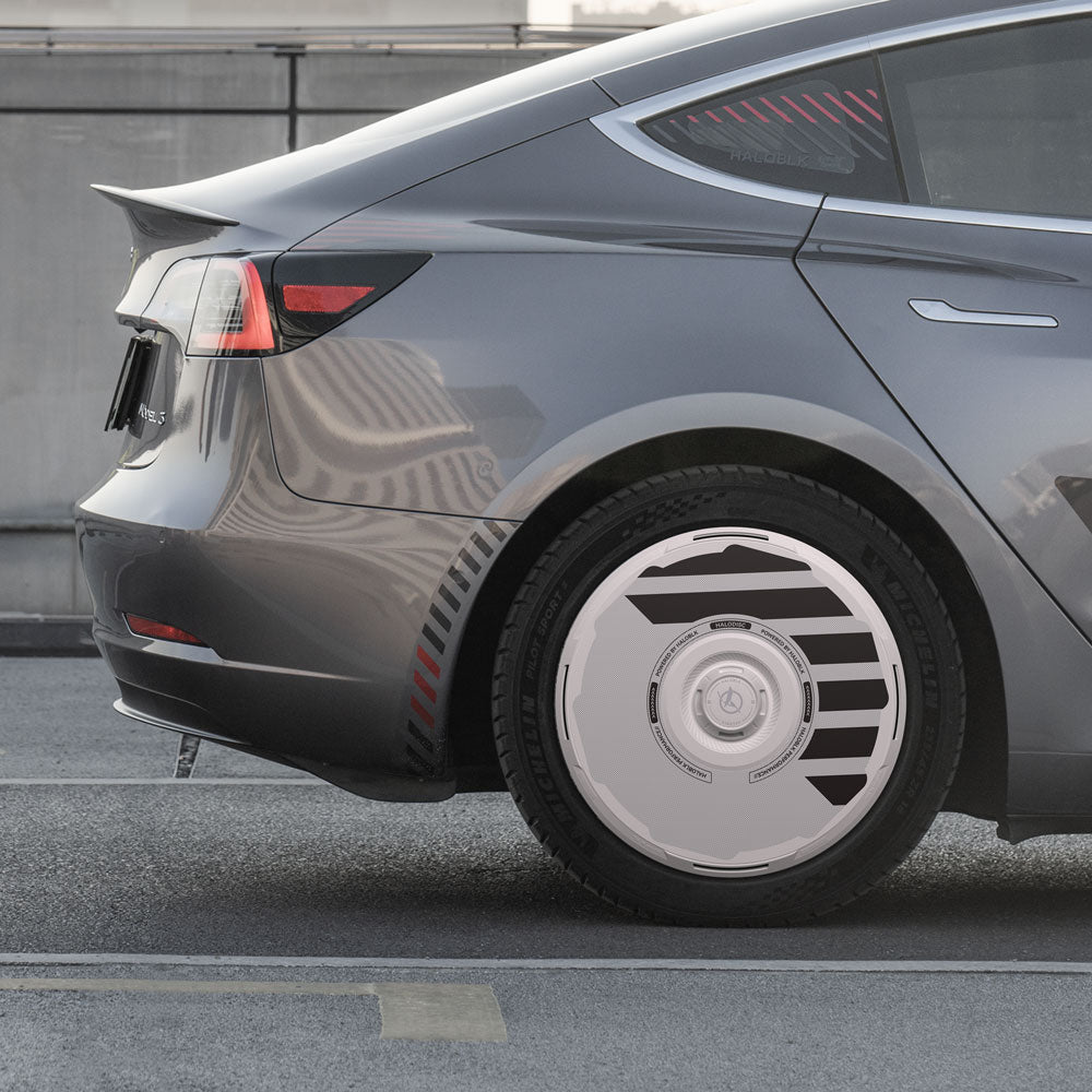 A close-up side view of a Tesla Model 3 (2017-2023) with HALODISC 2 Wheel Covers from HALOBLK Store, featuring unique aero design on 18" wheels, parked near a city street concrete barrier.