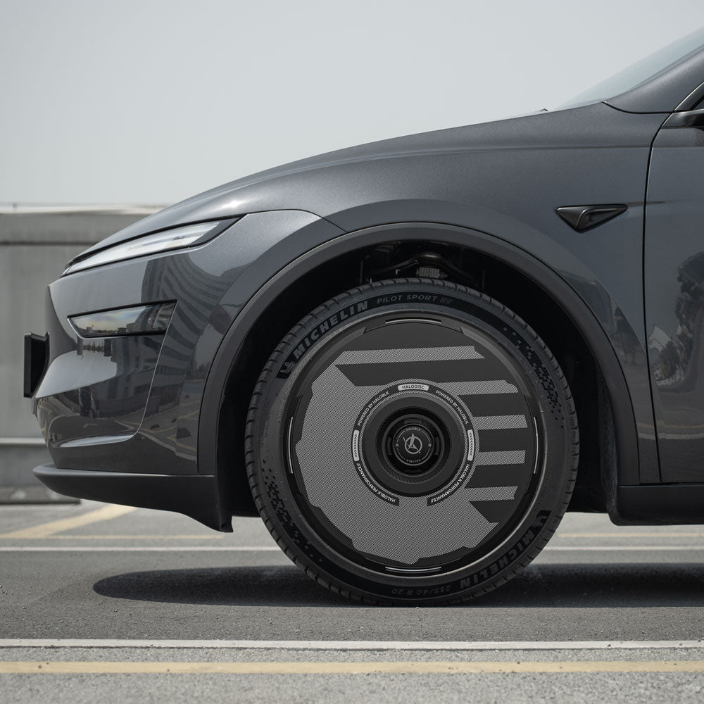 Close-up side view of a Tesla Model Y Juniper 19" Crossflow wheel fitted with HALODISC 2 wheel covers by HALOBLK Store, showcasing the unique, futuristic design, parked on a rooftop under a clear sky.