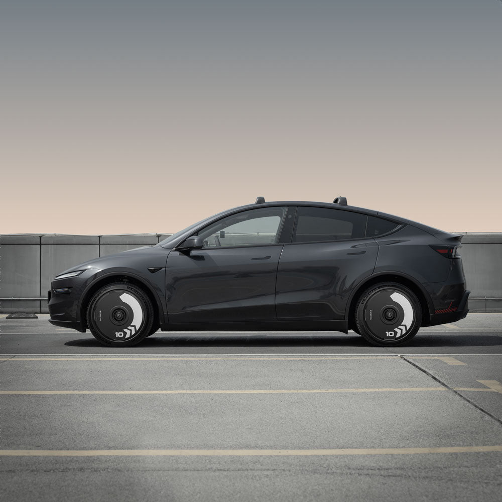 A Tesla Model Y with HALODISC 2 Wheel Covers (Arrow, Juniper 20" Helix 2.0) from HALOBLK Store is parked in an empty outdoor lot, set against a concrete barrier and a clear, softly gradient sky.