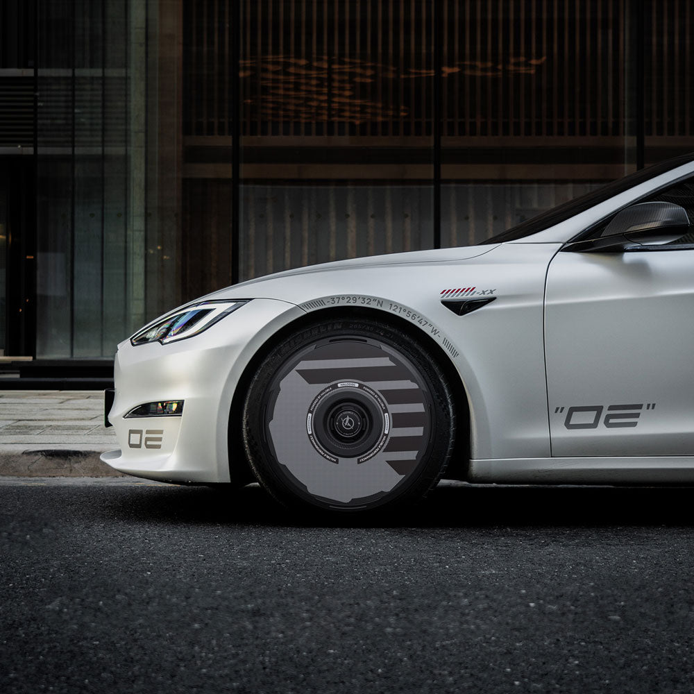A sleek white Tesla Model S with HALODISC 2 Wheel Covers for 21" Arachnid Wheels by HALOBLK Store is parked on the street, showcasing OE decals on the front bumper and door, with modern building windows in the background.