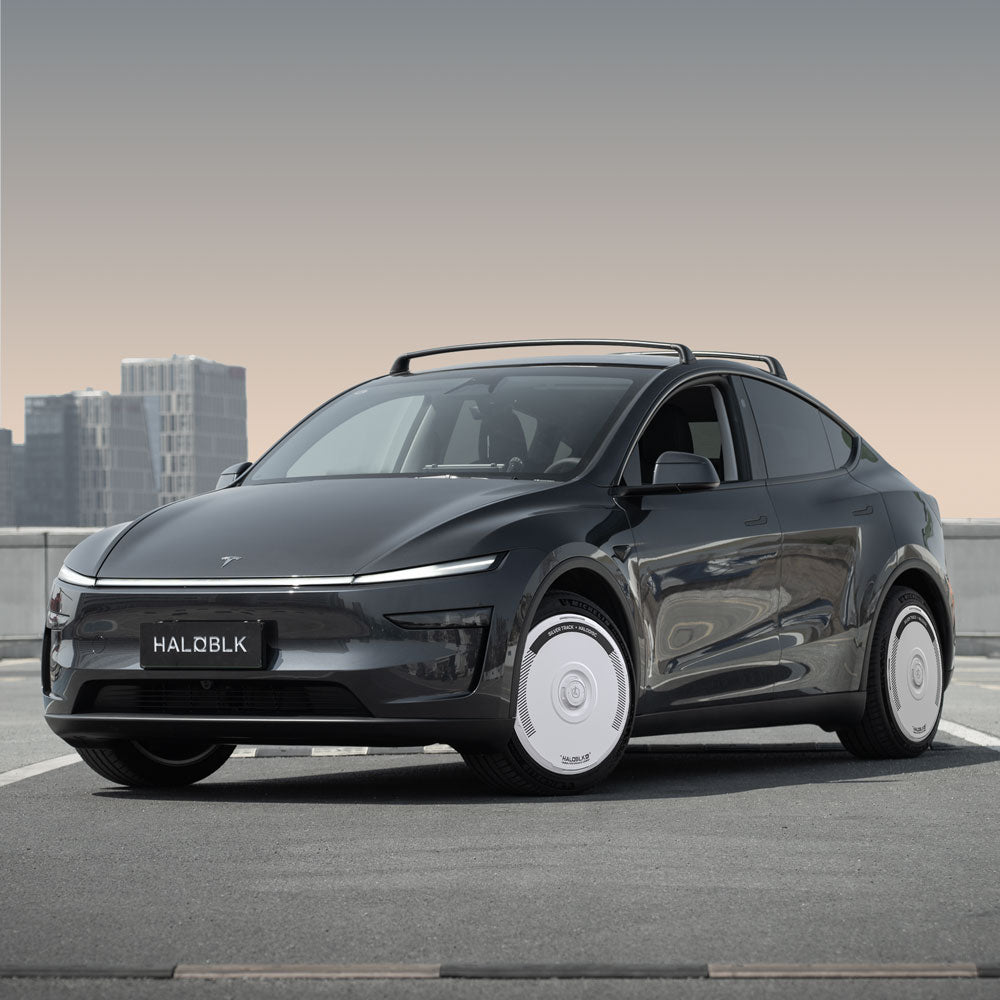 A Tesla Model Y with 20" Helix 2.0 wheels is parked on a rooftop, featuring HALODISC 2 Silver Track wheel covers from HALOBLK Store and a HALOBLK license plate, with modern buildings in the background.