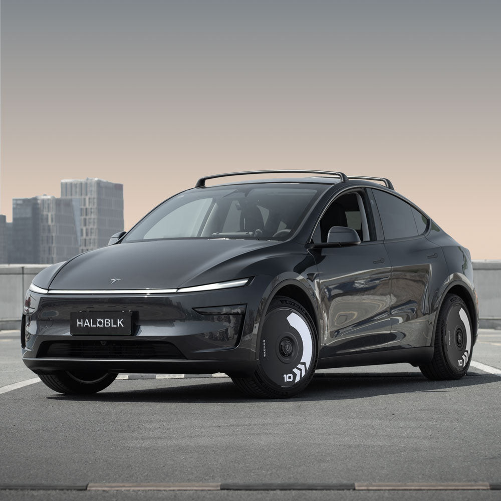 A sleek black Tesla Model Y with aerodynamic lines is parked on a rooftop against city buildings, featuring HALODISC 2 Wheel Covers for Juniper 20" Helix 2.0 wheels by HALOBLK Store, with distinctive front lights and Arrow design covers.