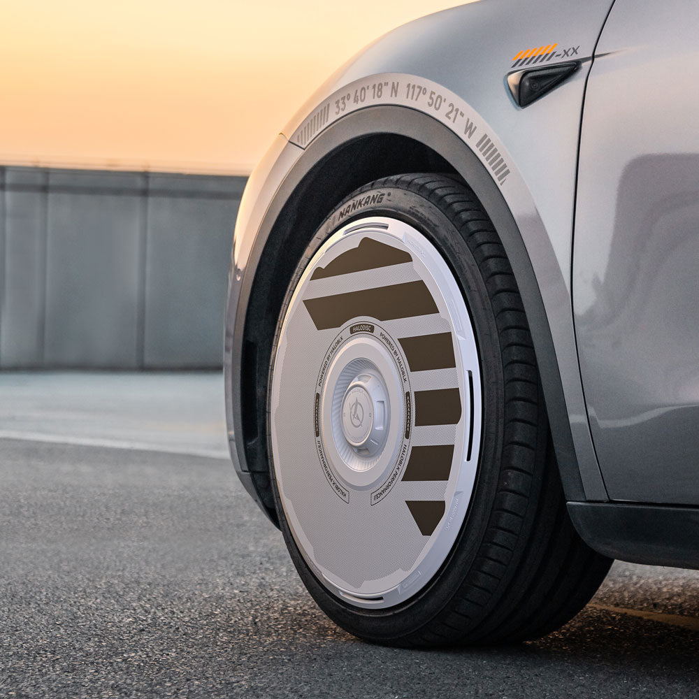 A close-up of HALODISC 2 Wheel Covers (by HALOBLK Store) on Tesla Model Y 20" Induction Wheels shows the futuristic white and brown design. The silver car sits outdoors at sunset, with coordinates above the wheel well.