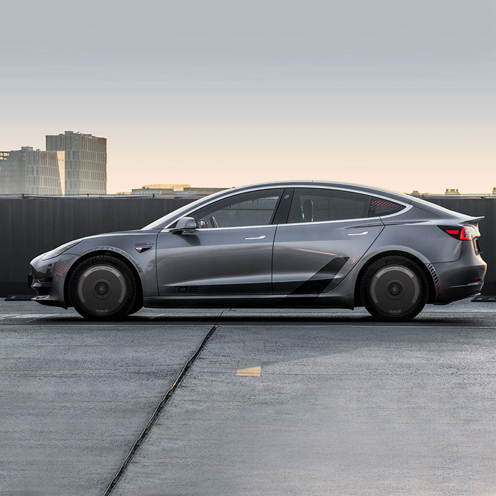 A Tesla Model 3 (2018-2023) with silver HALODISC 2 Wheel Covers by HALOBLK Store is parked on a rooftop at sunset, featuring 19" Stiletto Wheels, tinted windows, and city buildings in the background under a clear sky.