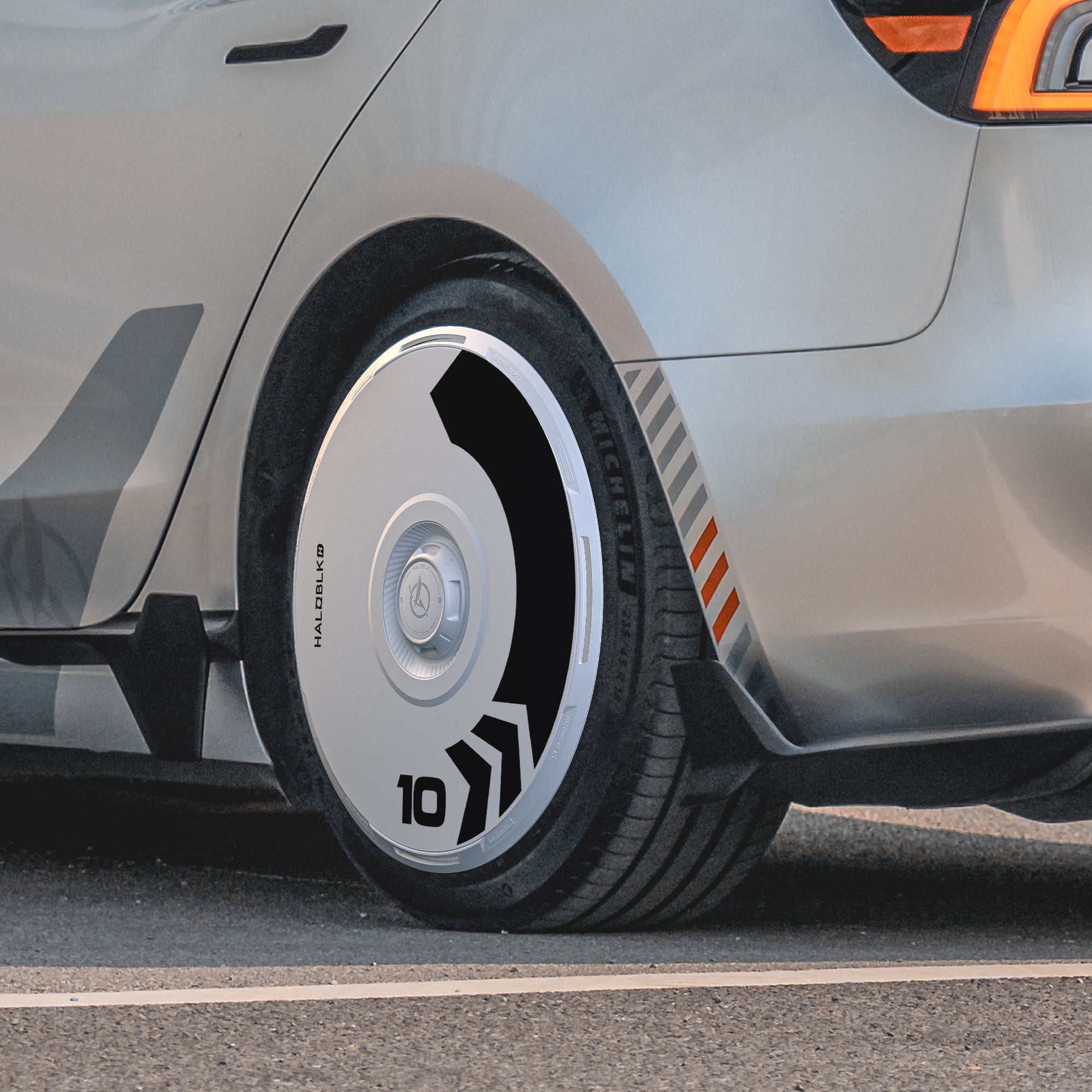 Close-up of a Tesla Model 3 Highland rear wheel with HALODISC 2 Wheel Covers by HALOBLK Store, featuring an Arrow design and sleek black and white geometric patterns, the number 10, and "HALO E4KD" on the cover.
