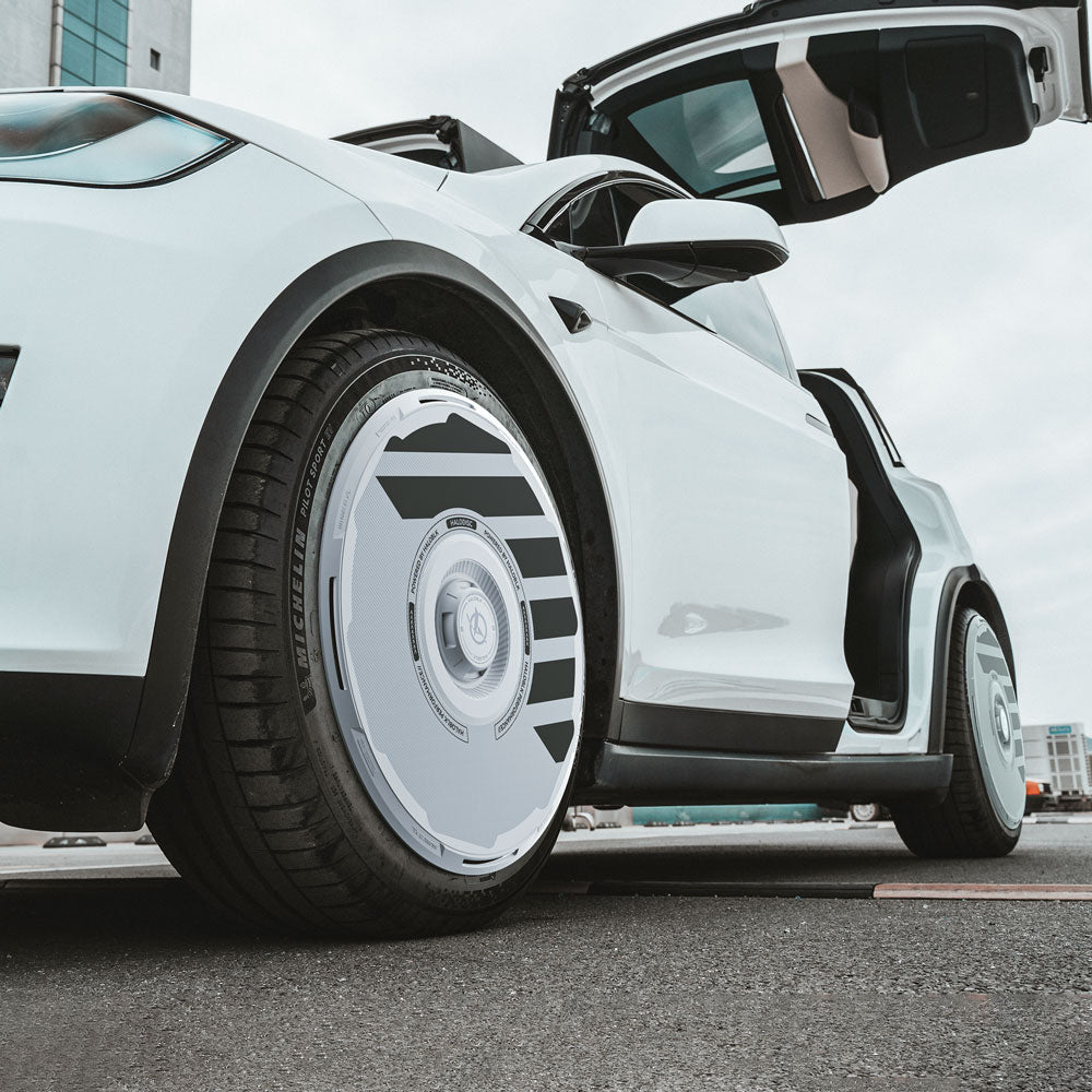 A close-up of a white Tesla Model X (2021-2025) with its rear falcon-wing door open, featuring HALODISC 2 Wheel Covers for 20" Perihelix Wheels by HALOBLK Store, parked on a city street.