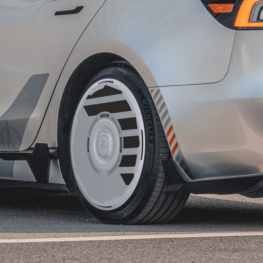Close-up of the rear wheel of a silver Tesla Model 3 Highland with HALODISC 2 Wheel Covers by HALOBLK Store, featuring a futuristic aerodynamic design and black-gray accents. Orange stripes highlight the tire sidewall and wheel arch.