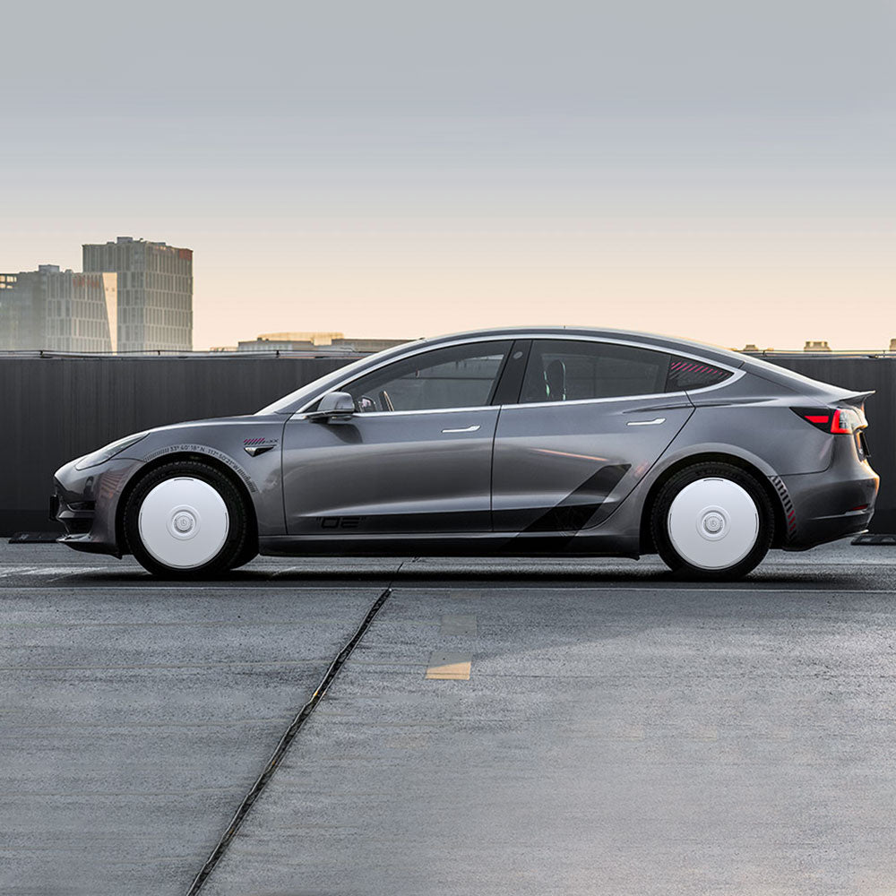 A gray Tesla Model 3 (2017-2018) with HALODISC 2 19" Wheel Covers from HALOBLK Store is parked on a rooftop at sunset, buildings in the background, shown in side profile with striking white wheel covers.