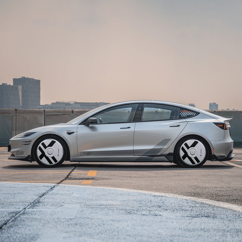 A Tesla Model 3 Highland with HALODISC 2 X-Factor geometric wheel covers from HALOBLK Store is parked on a rooftop, city skyline in the background beneath a hazy sky.
