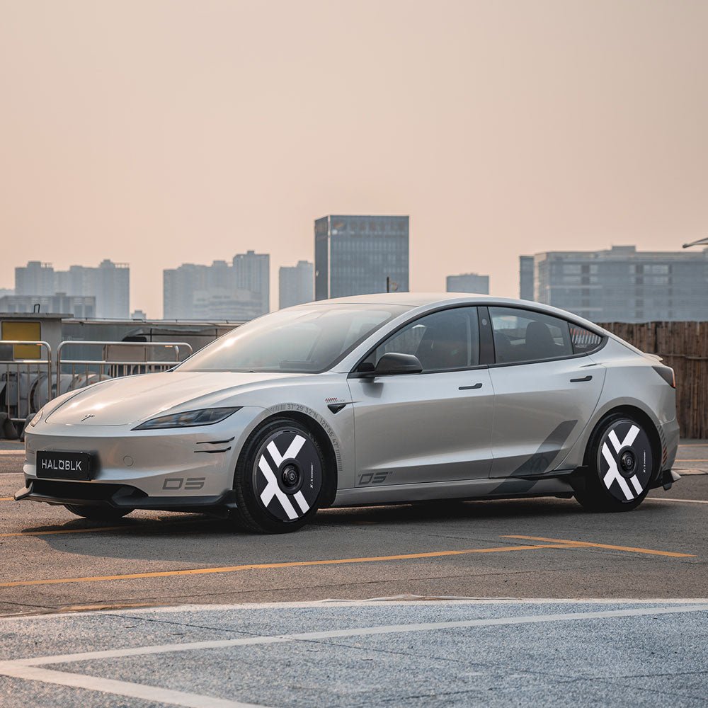 A Tesla Model 3 Highland with HALODISC 2 Wheel Covers (19" Nova Wheels) by HALOBLK Store, featuring modern silver design and black-and-white X-Factor wheel covers, is parked on a rooftop with a city skyline under a hazy sky.
