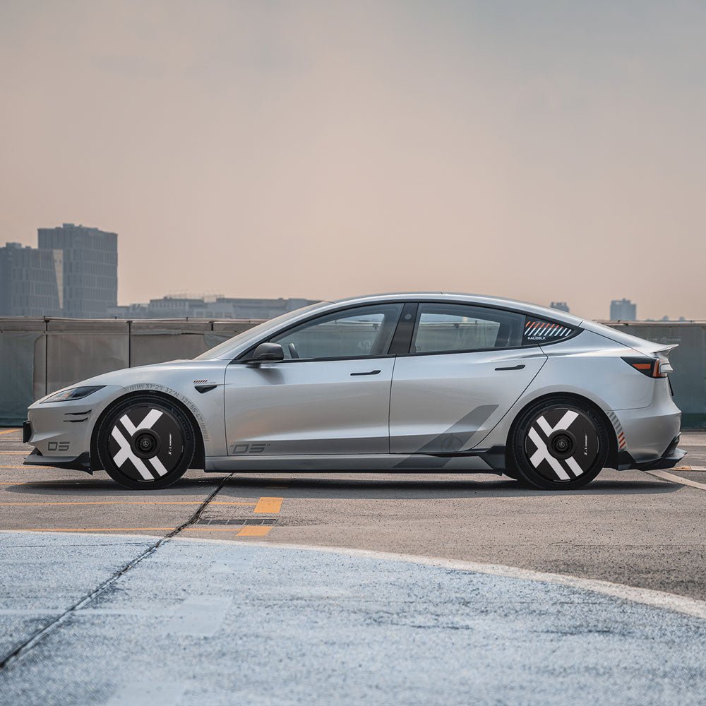 A Tesla Model 3 Highland with HALODISC 2 Wheel Covers for 19" Nova Wheels by HALOBLK Store, featuring a sleek silver finish and black-and-white X-Factor pattern, is parked on a rooftop with a city skyline in the background.