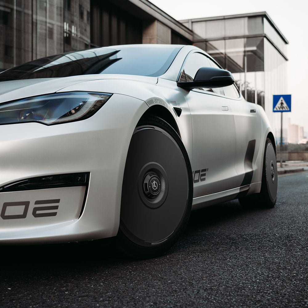 A white Tesla Model S with HALODISC 2 Wheel Covers by HALOBLK Store is parked on a city street near a glass building, with aerodynamic wheel covers and a pedestrian crossing sign visible in the background.