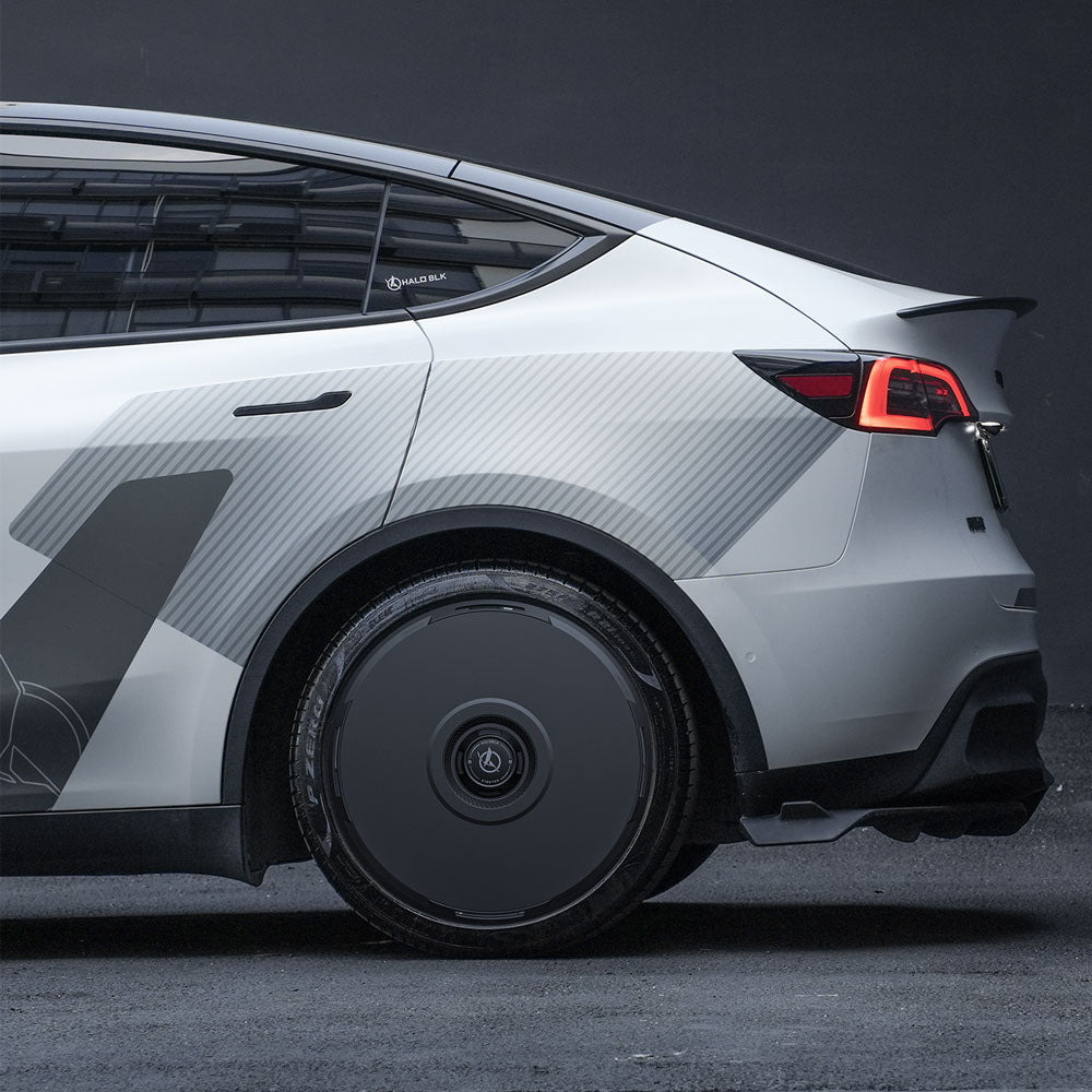 A close-up side view of a Tesla Model Y 21" with HALODISC 2 Wheel Covers by HALOBLK Store, featuring smooth black wheel covers (RTP), illuminated red tail light, and geometric decals on the silver EV body.